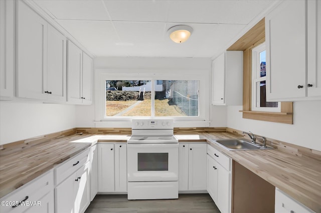 kitchen with white electric stove, white cabinetry, wood counters, and a sink