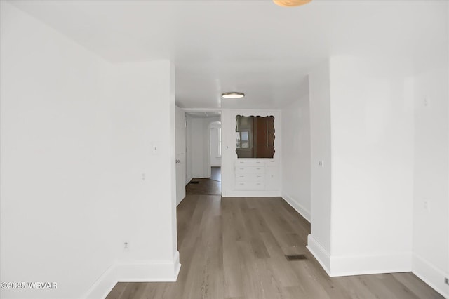 hallway featuring visible vents, baseboards, and wood finished floors