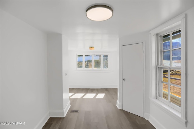 hallway with dark wood-style floors, plenty of natural light, baseboards, and visible vents