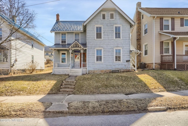 view of front of property featuring central air condition unit, a porch, a front yard, metal roof, and a chimney