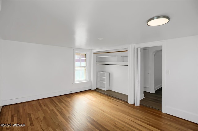 unfurnished bedroom with arched walkways, a closet, baseboards, and wood finished floors