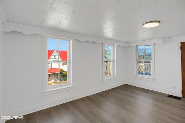 empty room with visible vents, wood finished floors, baseboards, and a wealth of natural light