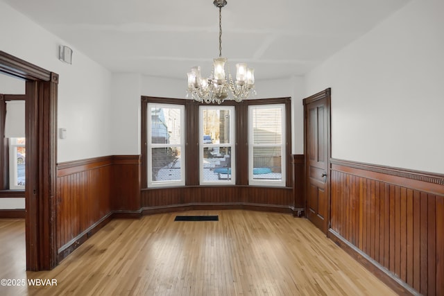 unfurnished dining area with wooden walls, a chandelier, and light hardwood / wood-style floors