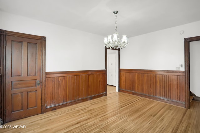 empty room with wood walls, light hardwood / wood-style flooring, and a notable chandelier