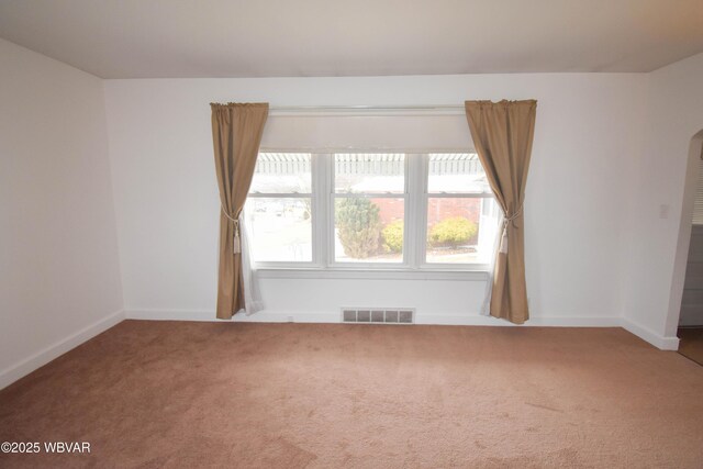 carpeted spare room featuring arched walkways, visible vents, and baseboards