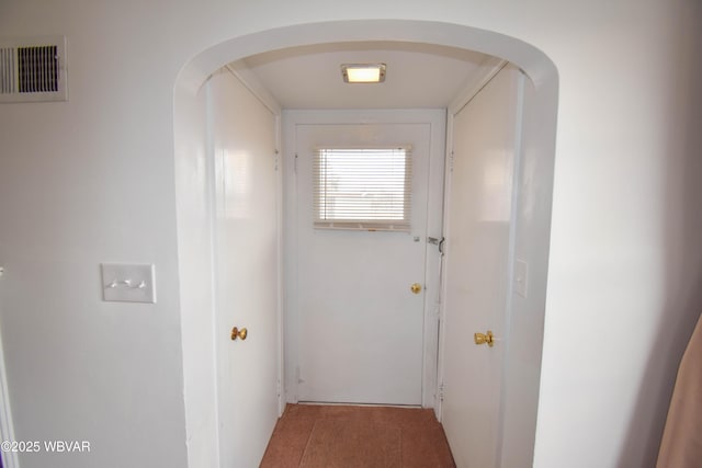 hallway featuring arched walkways, visible vents, and tile patterned floors