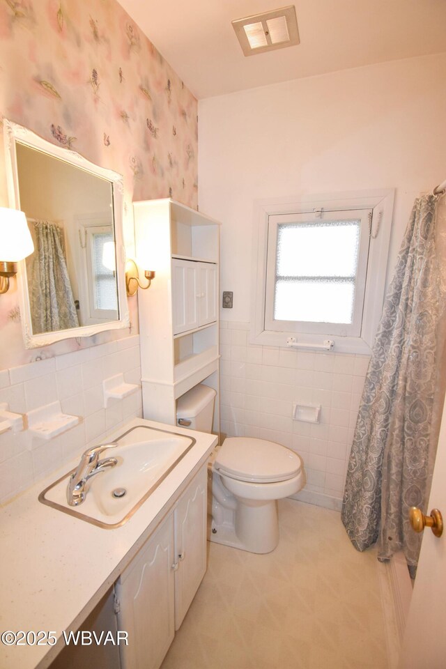 full bath with wallpapered walls, visible vents, toilet, vanity, and tile walls