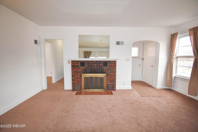 unfurnished living room with baseboards, visible vents, arched walkways, carpet floors, and a brick fireplace