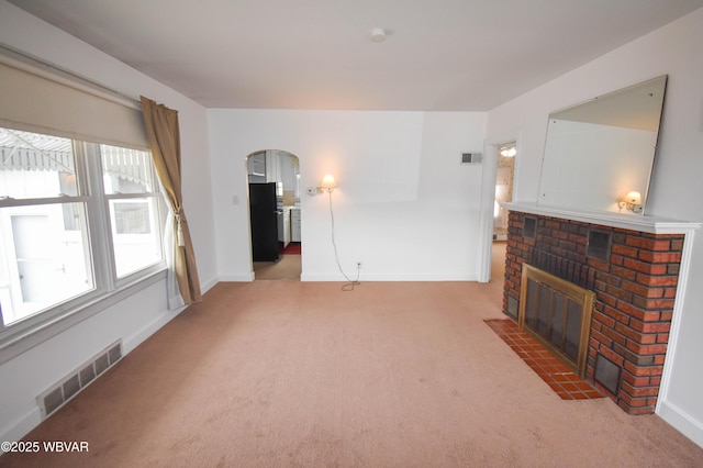 carpeted living area with a brick fireplace, baseboards, visible vents, and arched walkways