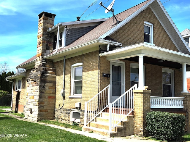 view of front of home with a porch, roof with shingles, fence, brick siding, and a chimney