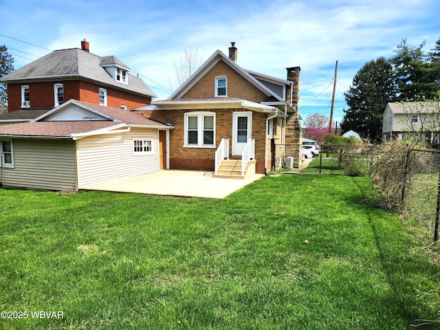 rear view of house featuring a lawn, a chimney, brick siding, fence, and a patio area