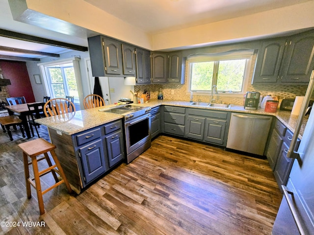 kitchen with dark wood-type flooring, sink, appliances with stainless steel finishes, kitchen peninsula, and a breakfast bar area