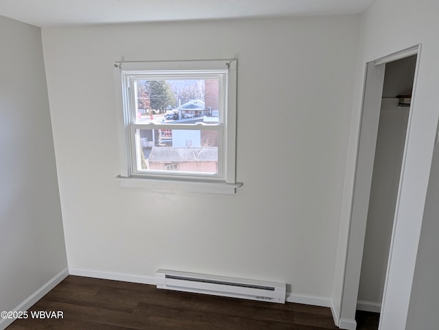 spare room featuring a baseboard heating unit and dark wood-type flooring