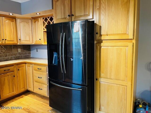 kitchen with black fridge, decorative backsplash, and light wood-type flooring