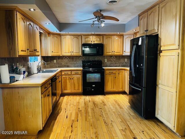 kitchen with sink, black appliances, light hardwood / wood-style flooring, ceiling fan, and backsplash