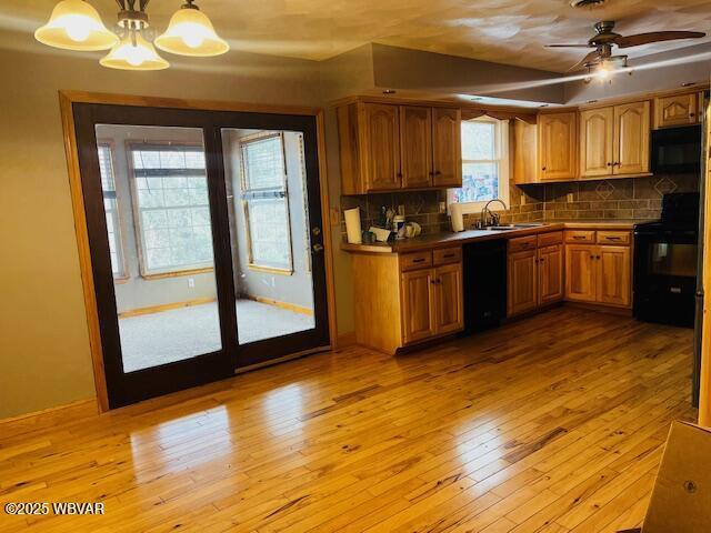 kitchen with pendant lighting, backsplash, light hardwood / wood-style flooring, and black appliances