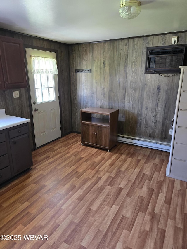 kitchen featuring baseboard heating, wood finished floors, a wall mounted AC, light countertops, and wood walls