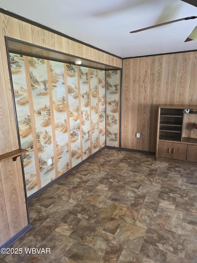 spare room featuring wood walls, baseboards, and a ceiling fan