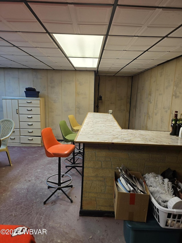 bar with concrete flooring, wood walls, and a paneled ceiling