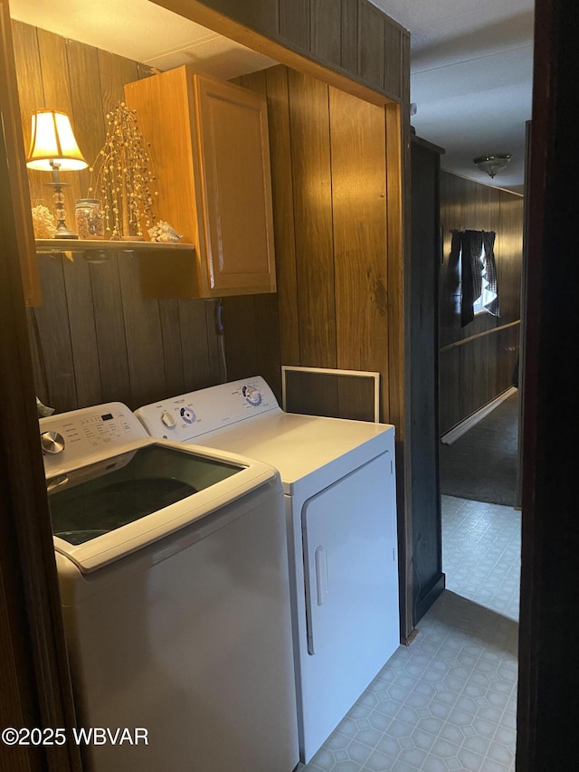 laundry room featuring cabinet space, light floors, washer and dryer, and wood walls