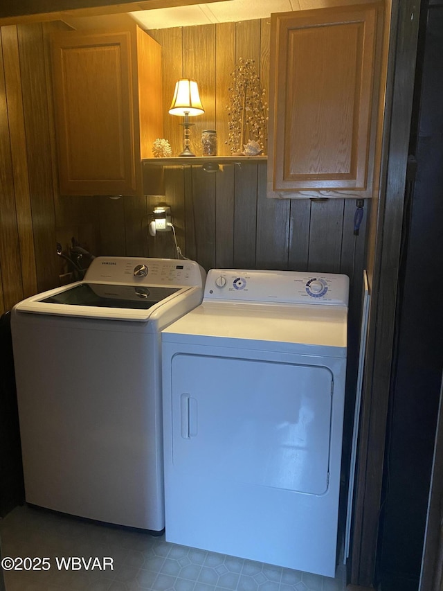 washroom with washing machine and clothes dryer, cabinet space, and wood walls