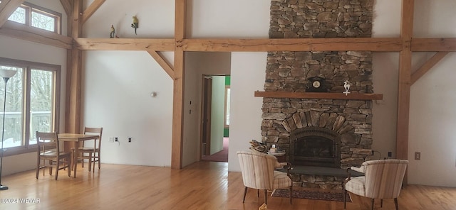 living room with high vaulted ceiling, a stone fireplace, and light hardwood / wood-style flooring