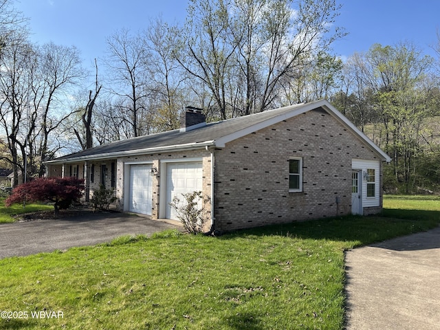 view of side of home with driveway, a chimney, brick siding, an attached garage, and a lawn