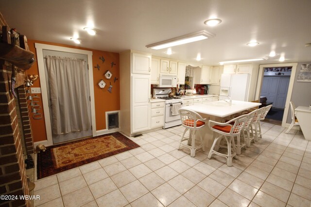 kitchen with a kitchen breakfast bar, white appliances, white cabinets, a kitchen island, and light tile patterned flooring