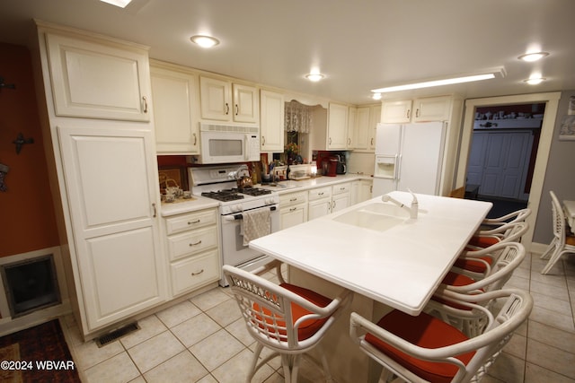 kitchen with a kitchen breakfast bar, sink, light tile patterned floors, and white appliances