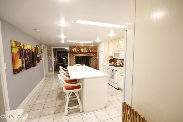 kitchen with a kitchen breakfast bar, white appliances, a kitchen island with sink, white cabinetry, and light tile patterned flooring