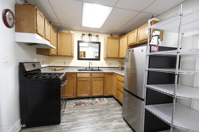 kitchen with gas stove, sink, a drop ceiling, stainless steel fridge, and light hardwood / wood-style floors