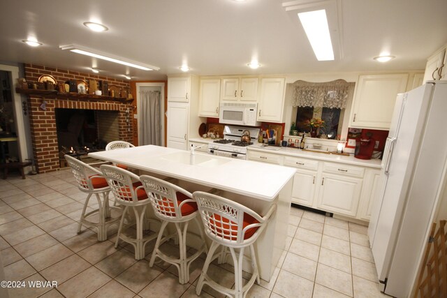 kitchen with a breakfast bar, white appliances, a center island with sink, light tile patterned flooring, and white cabinetry