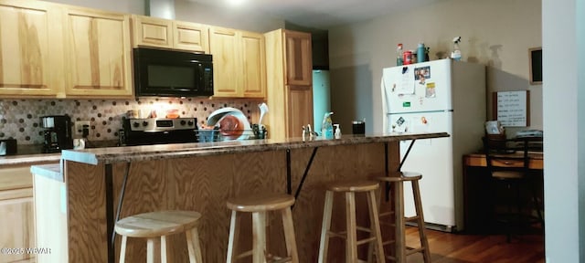 kitchen with electric range, tasteful backsplash, a breakfast bar area, freestanding refrigerator, and black microwave