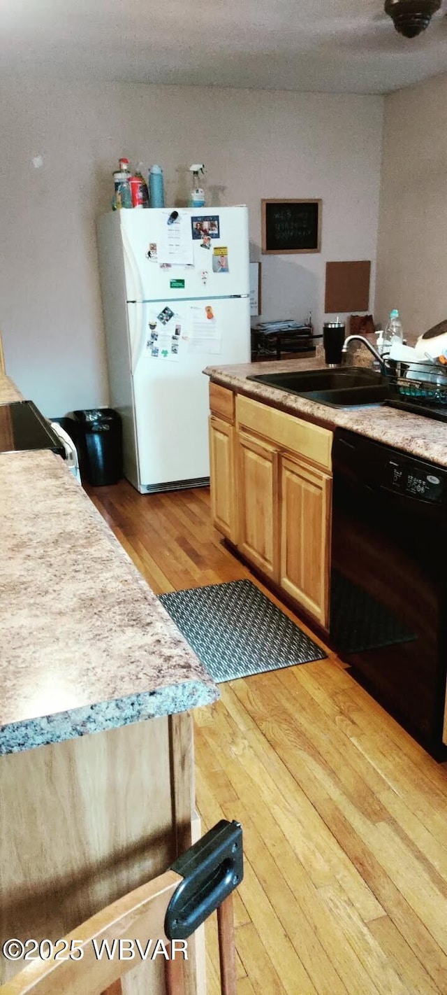 kitchen featuring light brown cabinets, light wood-style flooring, a sink, black dishwasher, and freestanding refrigerator