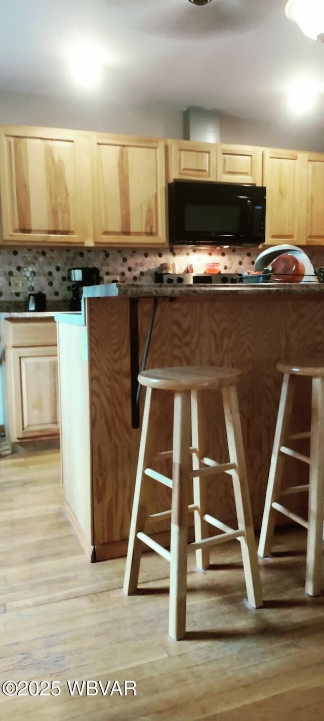 kitchen featuring tasteful backsplash, dark countertops, light wood-style floors, light brown cabinets, and black microwave