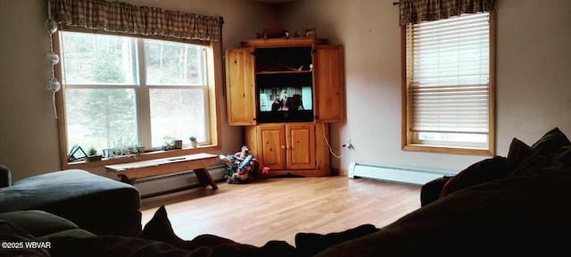 living area with a baseboard heating unit, baseboard heating, wood finished floors, and a wealth of natural light