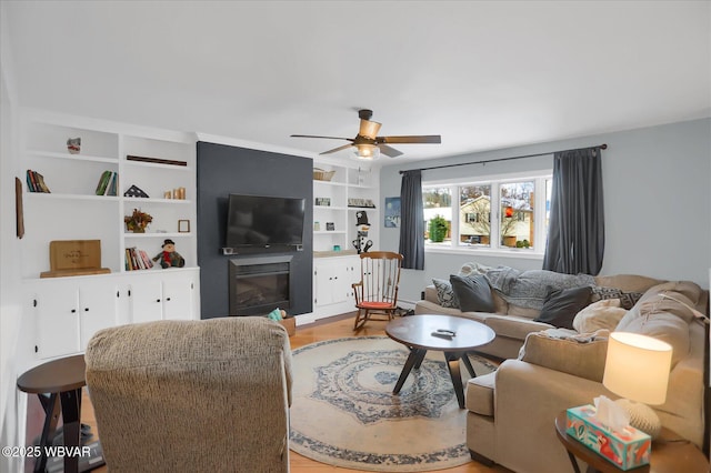 living room with ceiling fan, light hardwood / wood-style floors, built in features, and a fireplace