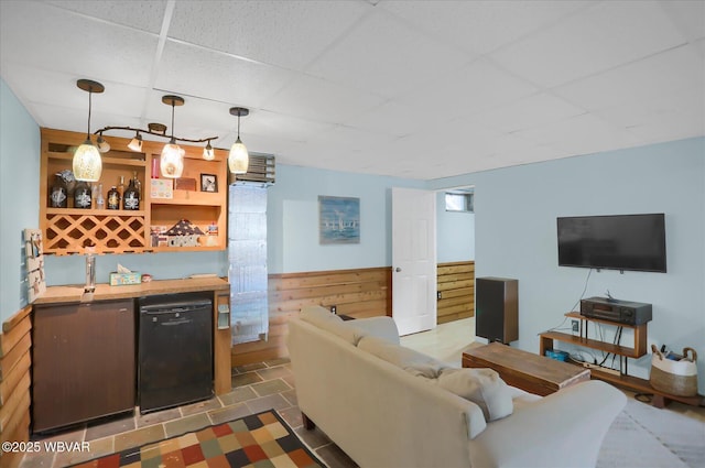 tiled living room featuring bar area, built in shelves, a paneled ceiling, and wooden walls