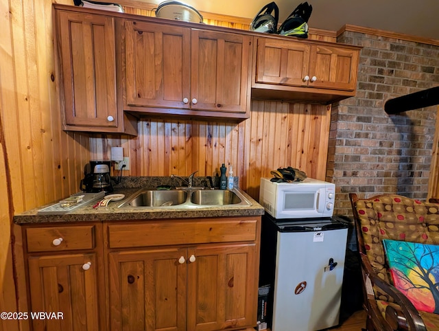 kitchen featuring sink, wooden walls, stainless steel refrigerator, and brick wall