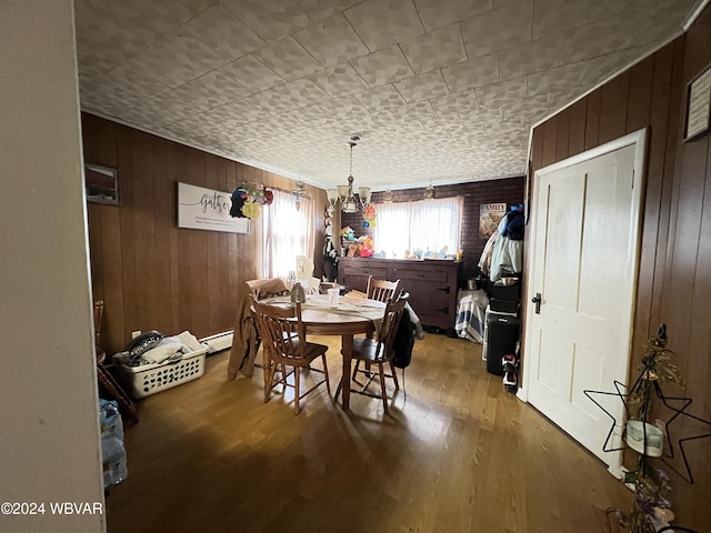 dining area with wood walls, hardwood / wood-style floors, a baseboard radiator, and a notable chandelier