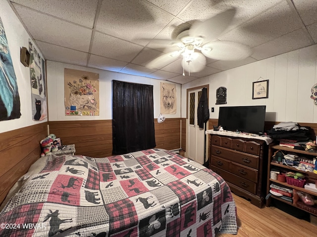 bedroom with a paneled ceiling, light hardwood / wood-style flooring, ceiling fan, and wood walls