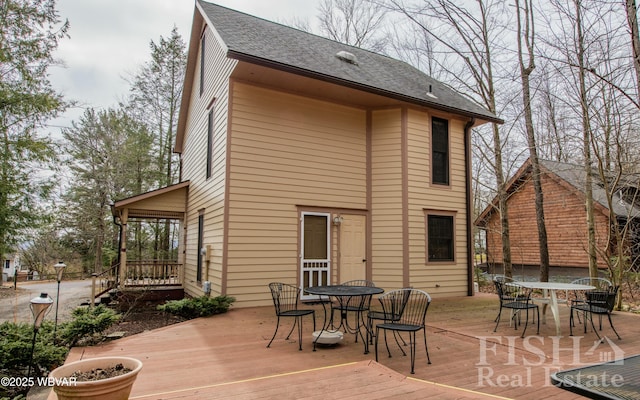 back of house with a deck, roof with shingles, and outdoor dining space