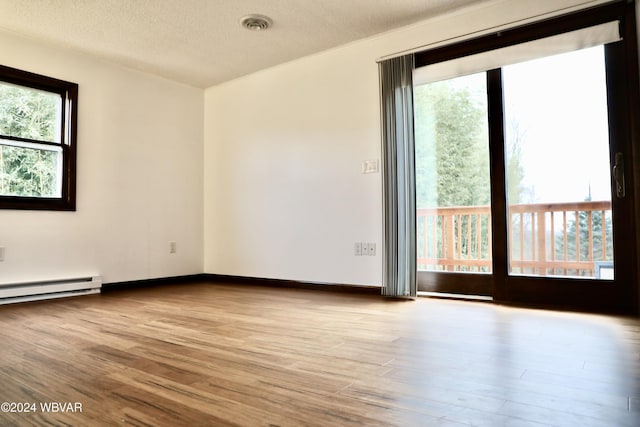 unfurnished room featuring light hardwood / wood-style flooring, a textured ceiling, and a baseboard heating unit