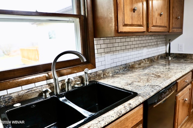 kitchen featuring backsplash, dishwasher, light stone countertops, and sink