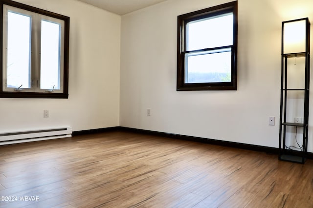 empty room with a wealth of natural light, light hardwood / wood-style floors, and a baseboard radiator