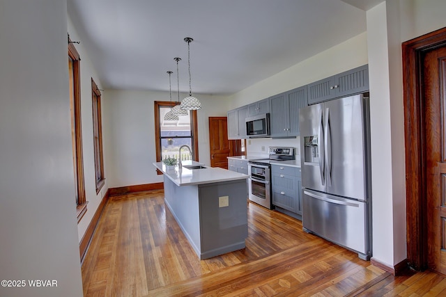 kitchen with decorative light fixtures, a sink, light countertops, appliances with stainless steel finishes, and gray cabinets