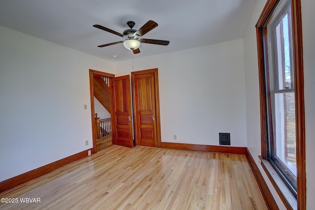 spare room featuring visible vents, light wood-style flooring, a ceiling fan, and baseboards