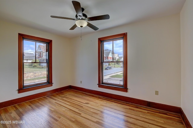 empty room with light wood-style flooring, a wealth of natural light, ceiling fan, and baseboards