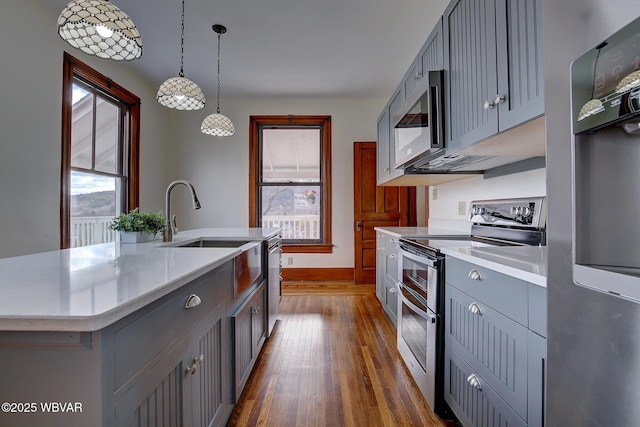 kitchen featuring appliances with stainless steel finishes, a kitchen island with sink, light countertops, gray cabinetry, and dark wood-style floors