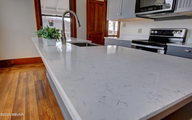 kitchen featuring baseboards, light stone countertops, stainless steel appliances, a sink, and wood finished floors